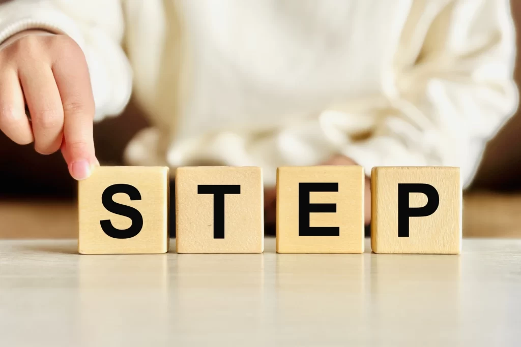 心の回復への段階的なプロセスを表現した「STEP」のアルファベットブロック。最初の一歩（S）を踏み出す手元のクローズアップ写真